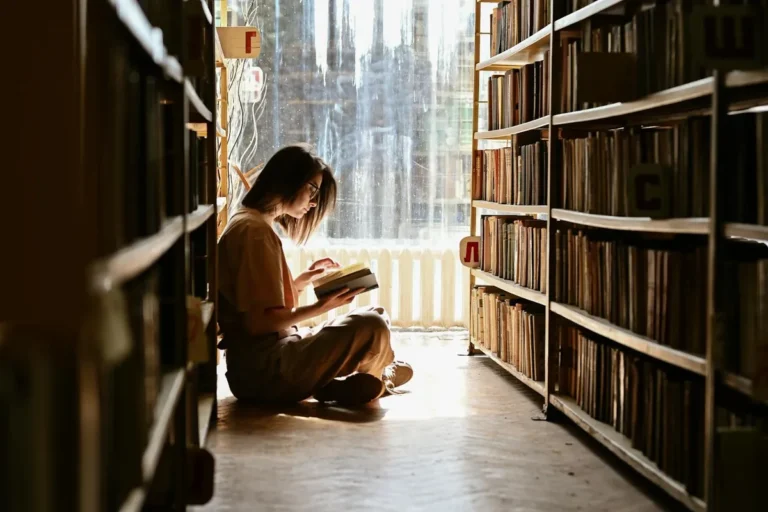 Young girl sitting on a library floor reading a book in calm sunlight, evoking focus and steady neurology