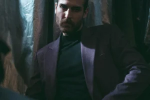 Contemplative man in a dark suit in dim light, embodying the tension between softness and strength