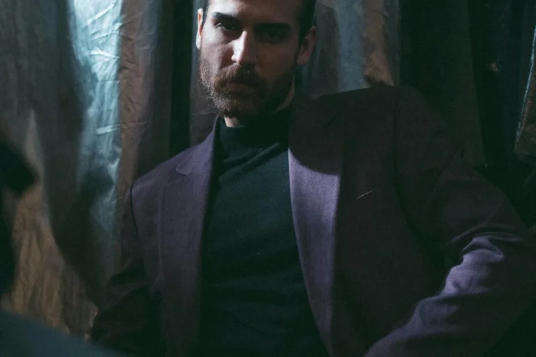 Contemplative man in a dark suit in dim light, embodying the tension between softness and strength